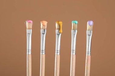 Açık kahverengi arkaplanda renk boyalı birçok fırça, yakın plan