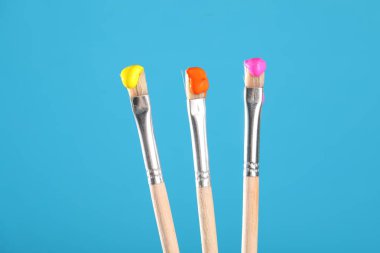 Açık mavi arkaplanda renkli üç fırça, yakın plan.