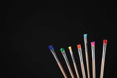 Siyah arka planda renk boyalı birçok fırça, yakın plan. Metin için boşluk