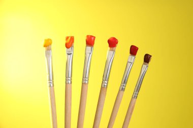 Sarı arkaplanda renk boyalı birçok fırça, yakın plan