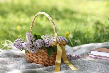 Yığınla kitap ve hasır sepet. Yeşil çimlerin üzerinde leylak çiçekleri, yakın plan.