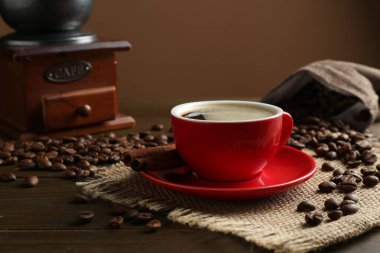 Aromatik kahve fincanda, fasulye, tarçın ve öğütücü ahşap masada, yakın plan.