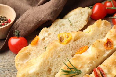 Cut delicious focaccia with tomatoes and rosemary on table, closeup