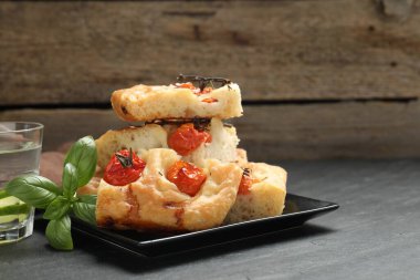 Domatesli, fesleğenli ve gri masadaki bir bardak suyla nefis Focaccia parçaları.
