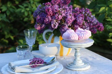 Güzel leylak çiçekleri, zephyrler, tabaklar, çatal bıçak takımı, bardaklar ve bahçede yanan mum.