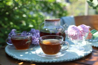 Fincanlarda romatik çay, çaydanlık, zephyr ve leylak çiçekleri bahçedeki ahşap masada, yakın plan.