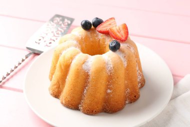 Pudra şekerli, dutlu ve pembe ahşap masadaki sunuculu lezzetli kek, yakın plan.