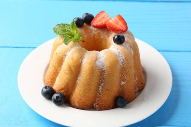 Açık mavi ahşap masada pudra şekerli ve dutlu Lezzetli kek, yakın plan.