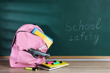 Sırt çantasında silah, bıçak ve kırtasiye malzemeleri var. Tahtanın yanındaki tahta masada. Okul güvenliği