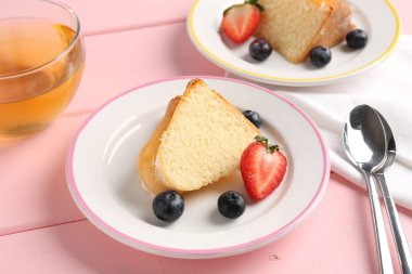 Lezzetli kek parçaları, böğürtlenli ve pembe ahşap masada çay, yakın plan.