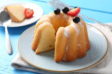 Açık mavi ahşap masada pudra şekerli ve dutlu Lezzetli kek, yakın plan.