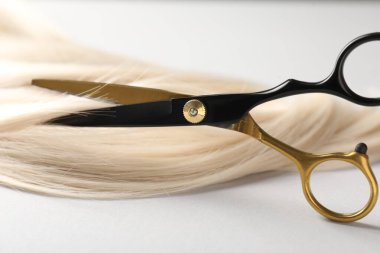 Açık gri arka planda makasla sarı saç tokası kesiliyor. Yakın plan.