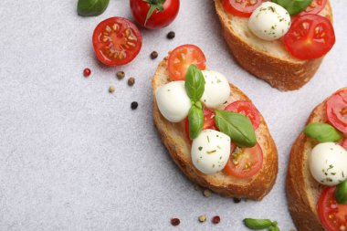 Peynirli mozzarella toplu lezzetli sandviçler, açık gri masada domates ve fesleğen, düz yatak. Metin için boşluk