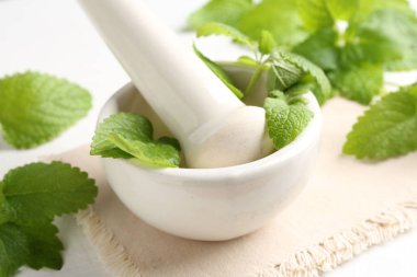 Taze limon merhemi yaprakları ve beyaz ahşap masada havan topuzu, yakın plan.