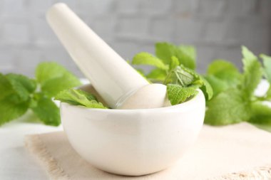 Taze limon merhemi yaprakları ve beyaz ahşap masada havan topuzu, yakın plan.