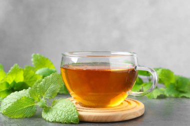 Cam bardakta Aromatik limon merhemi çayı ve gri desenli masada taze yapraklar.