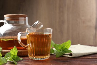 Cam fincanda aromatik limon merhemi çayı, çaydanlık ve ahşap masada taze yapraklar, metin için yer.