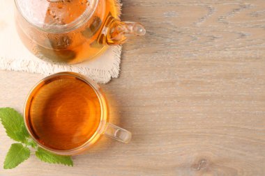 Cam fincanda aromatik limon merhemi çayı, çaydanlık ve ahşap masada taze yapraklar. Metin için boşluk