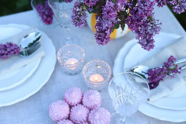 Güzel leylak çiçekleri, zephyrler, tabaklar, çatal bıçaklar, bardaklar ve yanan mumlar bahçede, yukarıdaki manzaranın üzerinde.