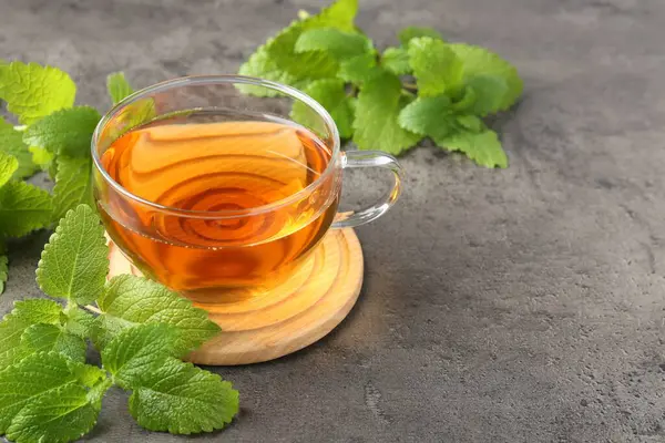 Cam bardakta Aromatik limon merhemi çayı ve gri desenli masada taze yapraklar, yakın plan. Metin için boşluk