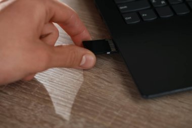 SD bellek kartını ahşap masada bilgisayara yerleştiren adam, yakın plan.