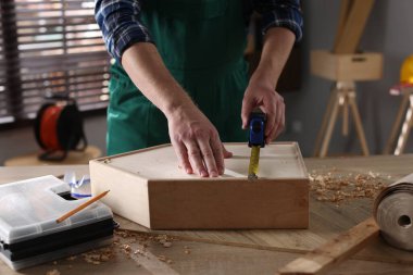 İçerideki masada bantlı ahşap kutuyu ölçen adam, yakın plan.