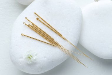 Akupunktur iğneleri, çakıl taşları ve çiçek tomurcukları beyaz masada, düz yatıyordu.