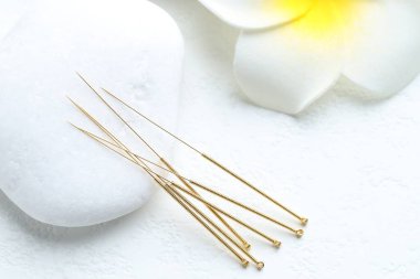 Beyaz arka planda akupunktur iğneleri, spa taşı ve çiçek, yakın plan.