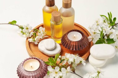 Spa ürünleri, yanan mumlar, çakıl taşları ve beyaz masadaki güzel çiçekli dallar, yakın plan.