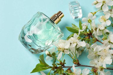 Bir şişe aromatik parfüm ve açık mavi arka planda güzel çiçekli dallar.