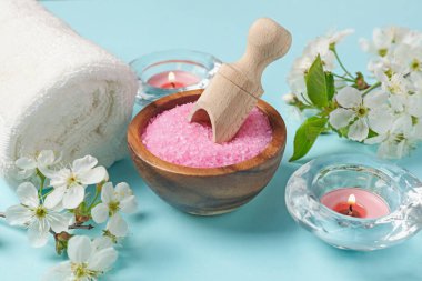 Deniz tuzu, yanan mumlar, havlu ve açık mavi arka planda güzel çiçekler içeren spa kompozisyonu, yakın plan.