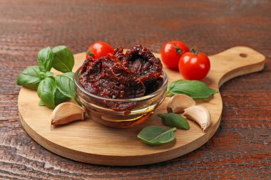 Lezzetli güneşte kurutulmuş domatesler, taze sebzeler, fesleğen ve sarımsak ahşap masada, yakın plan.