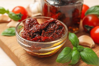 Lezzetli güneşte kurutulmuş domatesler, taze sebzeler, fesleğen ve sarımsak beyaz masada, yakın plan.