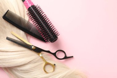 Açık pembe arka planda saç teli ve kuaför aletleri, düz yatış. Metin için boşluk