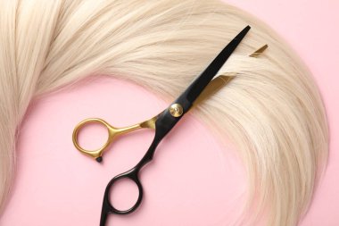 Açık pembe zemin üzerinde saç teli ve makas, üst görünüm