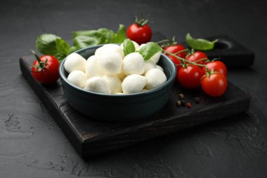 Lezzetli mozzarella peynir topları kasede, fesleğende, biberlikte ve domateslerde siyah masada, yakın plan.