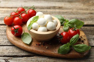 Lezzetli mozzarella peynir topları kasede, fesleğende, biberlikte ve domateslerde ahşap masada, yakın planda.
