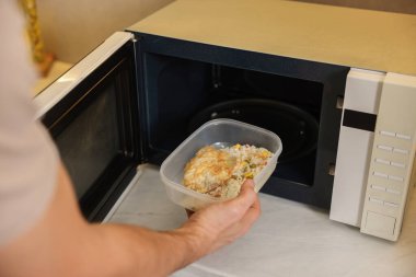 Yemek kabını mikrodalgaya koyan adam, yakın plan.