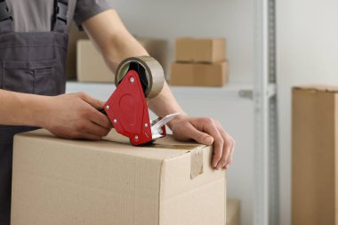 Karton kutuyu kapalı bir yere kapatmak için yapıştırıcılı bant kullanan bir adam. Metin için boşluk