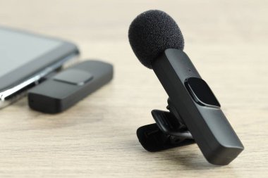 Lavalier mikrofon ve ahşap masada kablosuz alıcısı olan akıllı telefon.