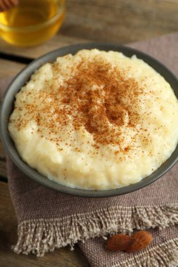 Tarçınlı lezzetli sütlaç, bal ve badem ahşap masada, yakın plan.