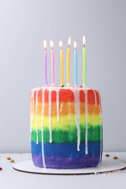 Enfes gökkuşağı doğum günü pastası yanan mumlar ve açık gri arka planda serpiştirmeler