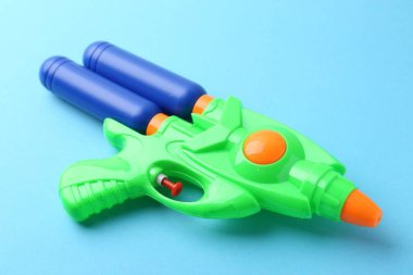 Açık mavi arkaplanda parlak plastik su tabancası, yakın plan.