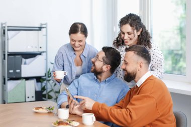 Ofiste öğle arasında iş arkadaşlarına akıllı telefondan bir şey gösteren bir adam.
