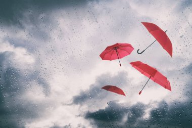 Bulutlu gökyüzünde uçan kırmızı şemsiyeler, ıslak pencereden manzaralı. Fırtınalı hava