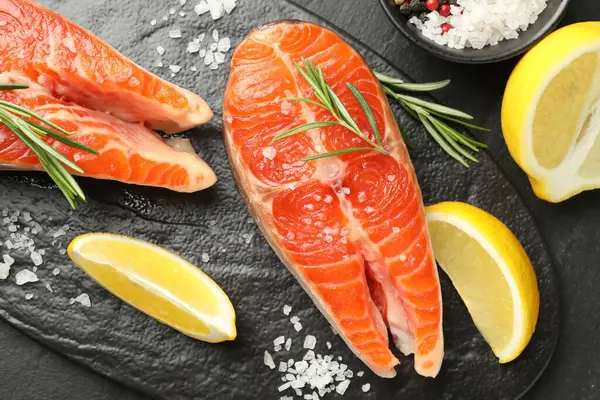 Deniz ürünleri. Somon bifteği, baharat ve limon siyah masada, düz yerde.