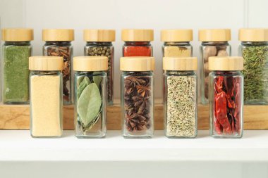 Beyaz masadaki kavanozlardaki farklı aromatik baharatlar, yakın plan.