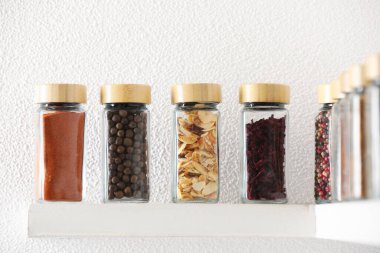 Beyaz raflardaki kavanozlardaki farklı aromatik baharatlar.