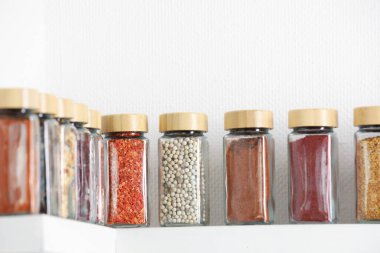 Beyaz raflardaki kavanozlardaki farklı aromatik baharatlar.