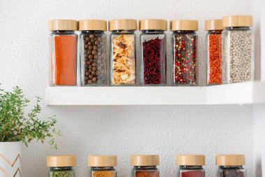 Beyaz raflardaki kavanozlardaki farklı aromatik baharatlar.